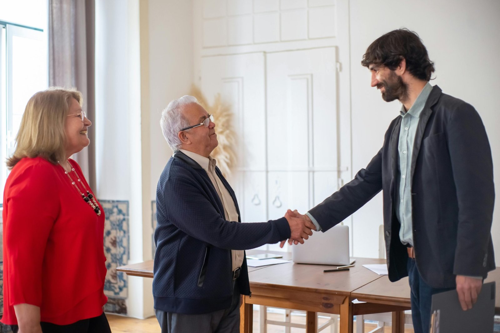 Elderly couple sealing a business deal with a handshake in a bright office.