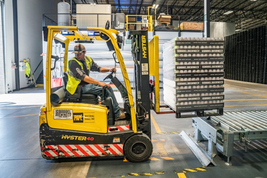 Personeel op locatie A warehouse worker maneuvers a forklift to transport crates for brewing company storage.