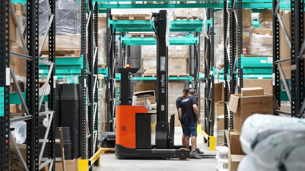 Personeel op locatie Warehouse scene featuring workers and a forklift navigating aisles for logistics and inventory management.
